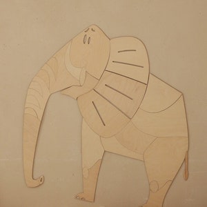 Op de afbeelding: Een houten olifantenwanddecoratie in een lichte kleur. De olifant heeft een segmentontwerp, met een lange slurf en grote oren. Het is gemonteerd op een neutrale muur boven kussens.