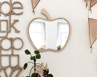 May include: A wooden alphabet wall sign with lowercase letters, an apple-shaped mirror, a woven basket with a green plant and a "wild one" sign, a wooden rainbow stacker, two wooden mushroom figures, and a large woven basket with a lid.