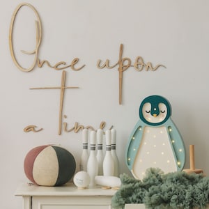 May include: A wooden wall sign reading Once upon a time, a multi-coloured fabric ball, a set of white bowling pins, and a light-up penguin lamp with a teal and light blue frame, featuring small glowing LED lights on its front panel.