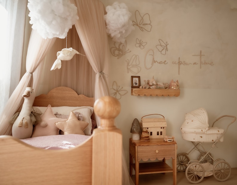 May include: A child's bedroom featuring a wooden bed with a beige canopy, a swan plush, and star-shaped pillows. The wall displays butterfly outlines and the text "Once upon a time" above a wooden shelf, a nightstand, and a vintage-style doll carriage.