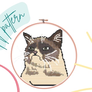 May include: Cross stitch pattern of a grumpy cat in a hoop. The cat is brown and white with a grumpy expression. The pattern is called "Grumpy Cat".