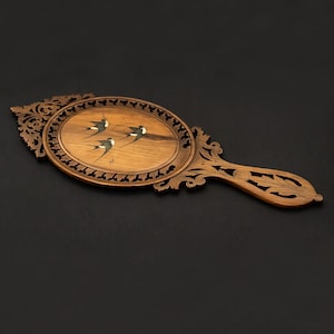 May include: An oval hand mirror with a carved wooden frame featuring intricate scrollwork and leaf patterns. The central panel displays a light wood inlay depicting three flying swallows in black and white, surrounded by a decorative openwork border.