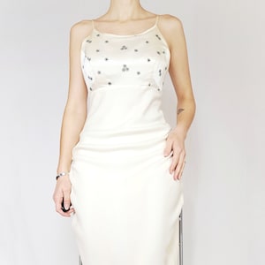 May include: A white satin dress with a beaded bodice and a fitted silhouette. The dress has a scoop neckline and thin straps.