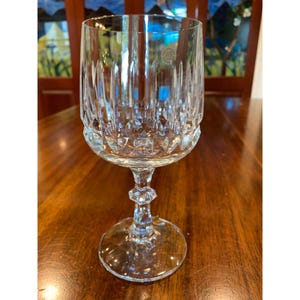 May include: A clear glass wine glass with a cut crystal design. The glass has a tall, slender stem and a wide, round bowl.