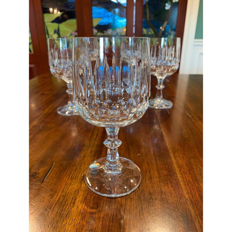 May include: Set of four clear glass wine glasses with a cut crystal design. The glasses have a tall, slender stem and a round bowl.