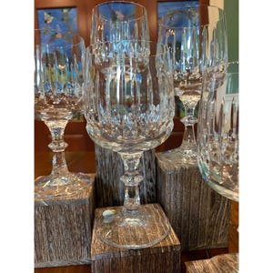 May include: Set of six clear glass wine glasses with a cut crystal design. The glasses are displayed on wooden blocks.