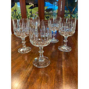 May include: Set of six clear crystal wine glasses with a cut glass design. The glasses have a tall, slender stem and a round bowl.