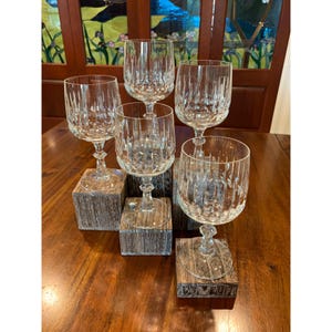 May include: Five clear glass wine glasses with a cut crystal design are displayed on wooden blocks. The glasses are arranged in a staggered pattern.