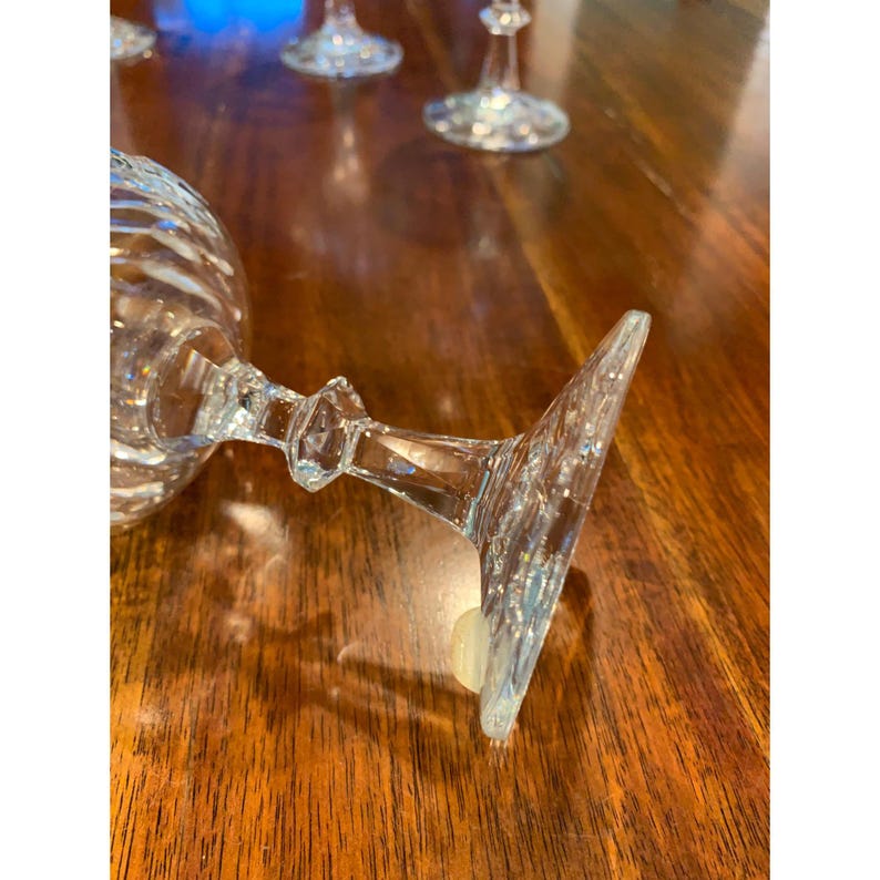 May include: A set of five clear glass wine glasses with a decorative cut pattern on the bowl and stem. The glasses are arranged on a wooden table.