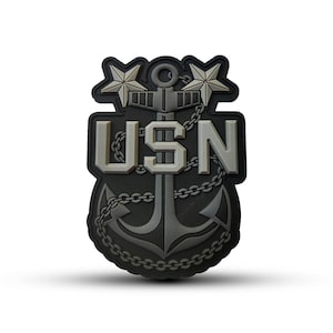 May include: A black and gray embroidered patch with a silver anchor, two stars, and the text "USN".