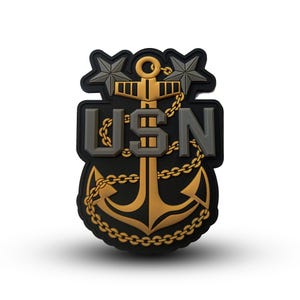May include: A black and gold embroidered patch with a gold anchor, two gold stars, and the text "USN" in gray.
