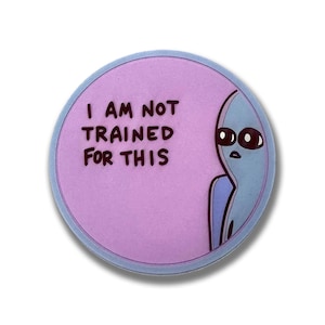 May include: A round sticker with a light purple center and a blue border. The text "I AM NOT TRAINED FOR THIS" is printed in black. A blue alien with large black eyes is on the right side of the sticker.