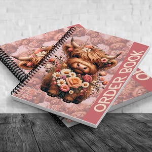 May include: Two spiral-bound order books with a floral Highland cow design. The cover features a brown cow adorned with flowers and the text "ORDER BOOK" in white on a red background. The background has a pink floral pattern.