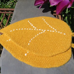 May include: Two mustard yellow knitted pot holders with white stitching in the shape of a leaf.