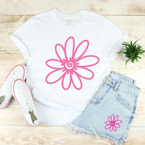 May include: A white t-shirt with a pink daisy design. The daisy has a swirl in the center. A pair of white sneakers and denim shorts with a smaller pink daisy design are also pictured.