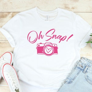 May include: White t-shirt with a pink camera and the text "Oh Snap!" printed on it.