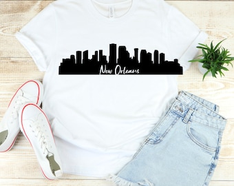 May include: White t-shirt with a black silhouette of the New Orleans skyline and the text "New Orleans" printed on the front.