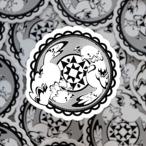 Puede incluir: Pegatina en blanco y negro con un diseño estilizado de dos pájaros con un patrón de estrella en el centro. La pegatina tiene un borde festoneado.