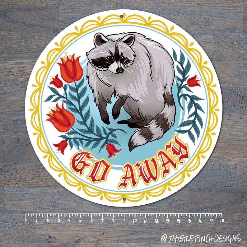 May include: A round, white sign with a gold border and floral design. A raccoon sits in the center of the sign with the words "GO AWAY" in red letters.