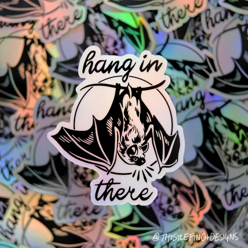 Op de afbeelding: Een holografische sticker met een zwart-witte illustratie van een vleermuis die ondersteboven hangt met de tekst "hang in there".