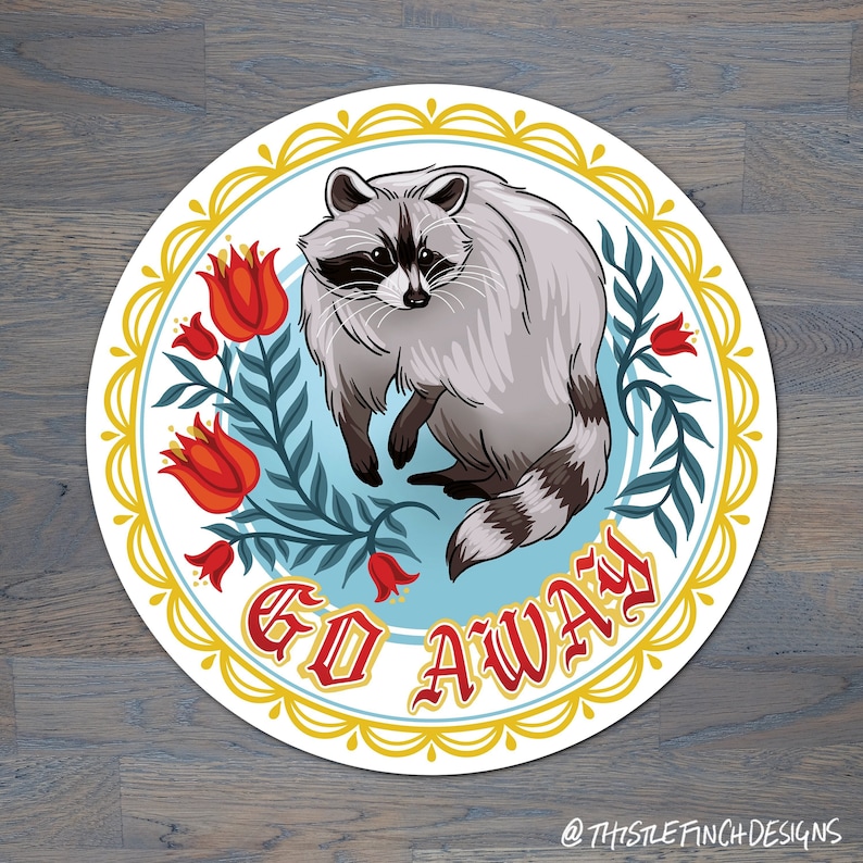 May include: A round sticker with a blue background and a white border. The sticker features a cartoon raccoon with a red, white, and blue floral design. The text "GO AWAY" is written in red letters.