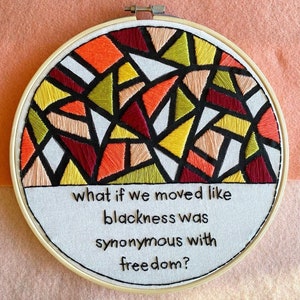 May include: Embroidered hoop art with a colorful geometric pattern in shades of red, orange, yellow, and green. The text "what if we moved like blackness was synonymous with freedom?" is written below the pattern.