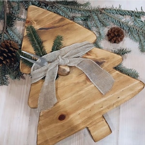 May include: A wooden Christmas tree-shaped serving board with a natural wood finish. The board is decorated with a hessian ribbon and a metal serving fork.