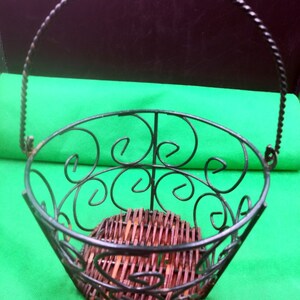 May include: A black metal wire basket with a woven bottom and a twisted wire handle.