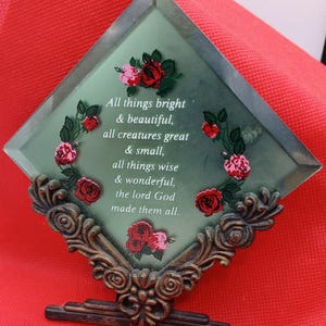 May include: A green glass diamond-shaped plaque with a gold metal stand. The plaque has a floral design with red roses and the text "All things bright & beautiful, all creatures great & small, all things wise & wonderful, the lord God made them all."