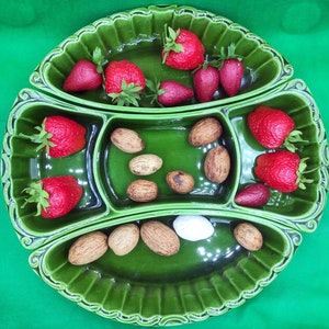 Puede incluir: Un plato de servir de cerámica verde con cuatro secciones. El plato está lleno de fresas, nueces y un objeto blanco. El plato tiene un borde festoneado decorativo.