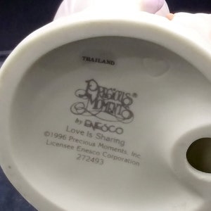以下が含まれることがあります： 手をつないでいるカップルの白い磁器の置物で、台座に「Precious Moments」と「Love Is Sharing」の文字が書かれています。この置物はタイ製で、272493という番号が付けられています。