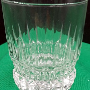 May include: A clear glass tumbler with a textured, diamond-shaped pattern. The glass has a wide base and a straight, cylindrical body.