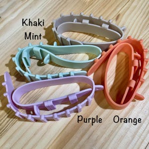 May include: Four colorful, plastic, oval-shaped cookie cutters in khaki, mint, purple, and orange. The cookie cutters have a decorative edge and the names of the colors are written on the image.