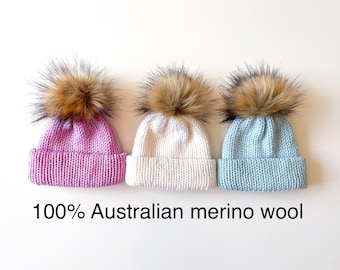 May include: Three knitted hats with faux fur pom-poms. The hats are pink, white, and light blue. 100% Australian merino wool.