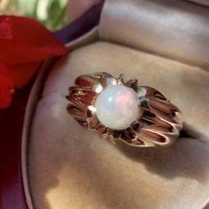 May include: A gold ring with a white opal gemstone set in a textured band. The ring is in a red velvet ring box.