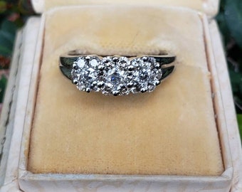 May include: A silver ring with three clusters of small diamonds set in a band.