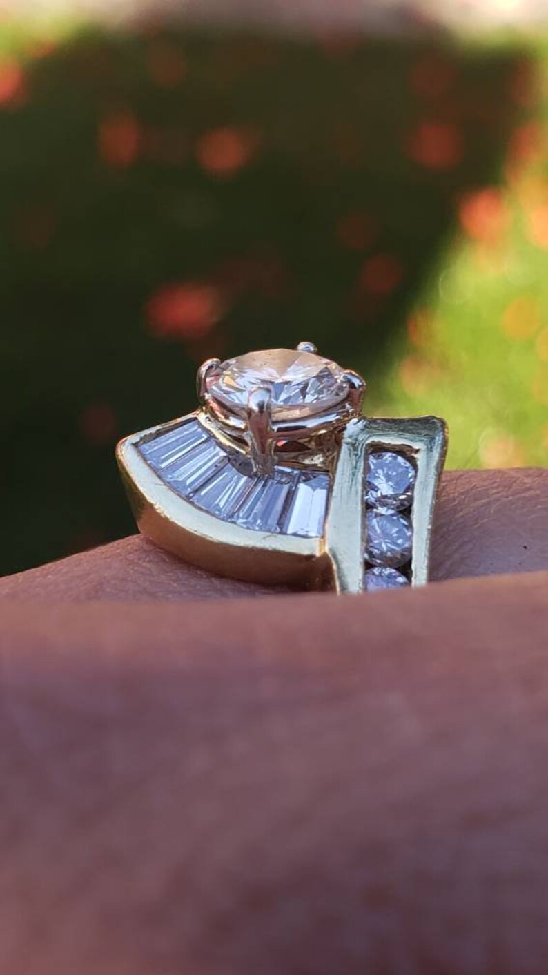 May include: A gold ring with a large round diamond in the center and smaller diamonds on the band. The ring is set in a fan shape with baguette diamonds.