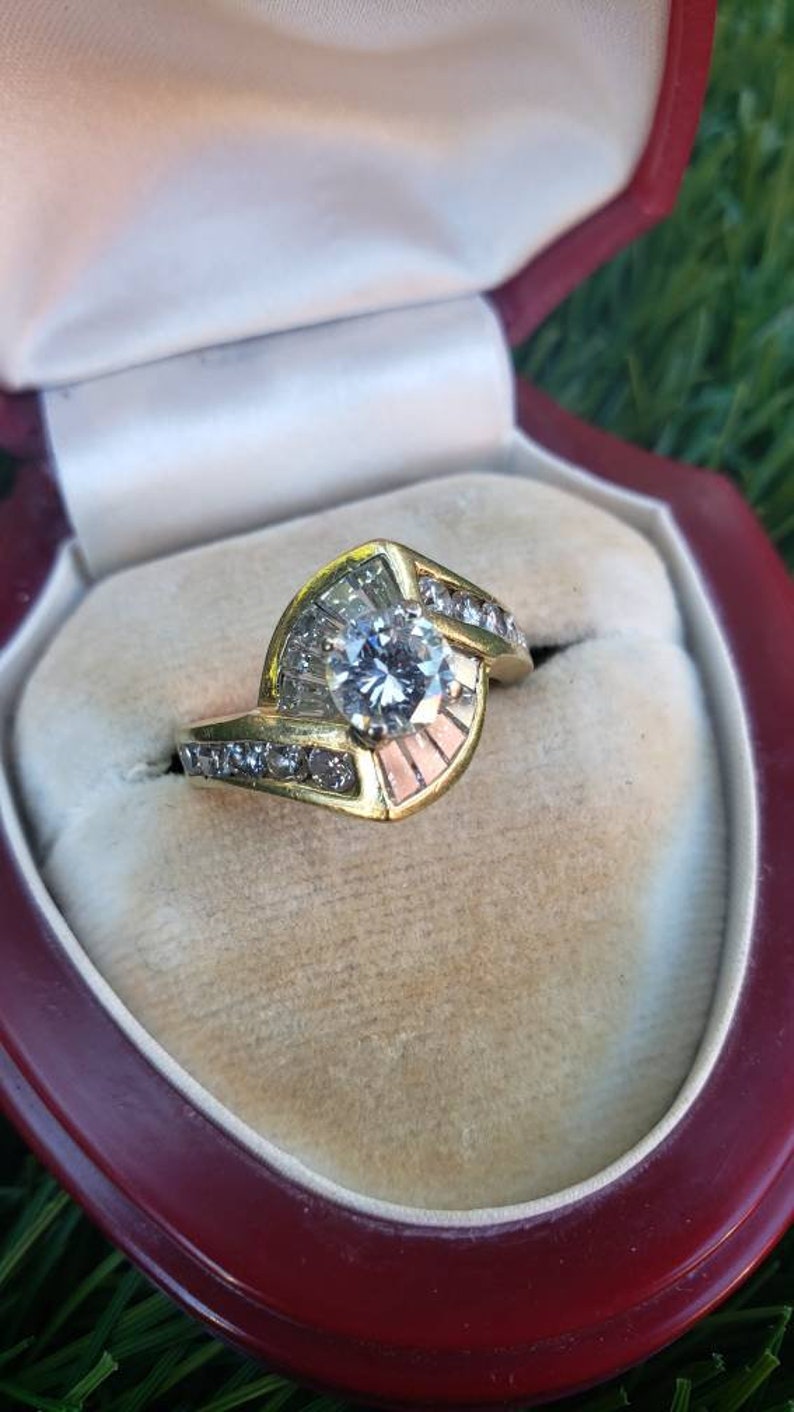May include: A gold engagement ring with a large, round, clear diamond center stone. The ring has a unique design with smaller diamonds set in a curved band.