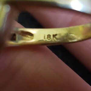 May include: Close-up of a gold ring with a row of small diamonds. The ring is marked "18K" on the inside.