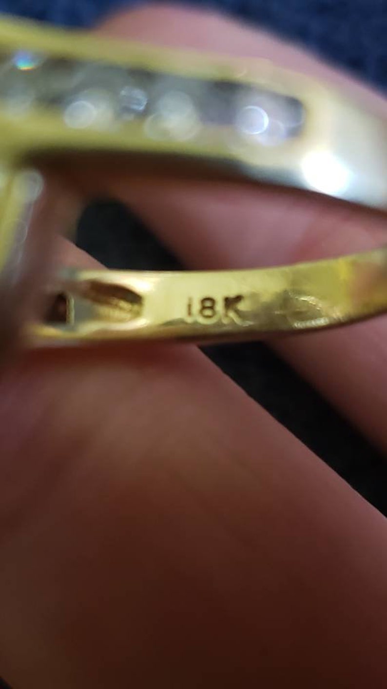 May include: Close-up of a gold ring with a row of small diamonds. The ring is marked "18K" on the inside.