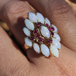 May include: A gold ring with a cluster of white opals and red rubies. The ring is set in a floral design.