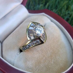 May include: A gold ring with a large round diamond surrounded by smaller diamonds in a leaf-shaped setting. The ring is in a red velvet ring box.