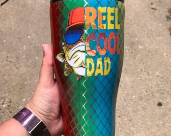 Könnte beinhalten: Ein roter, grüner und blauer Edelstahlbecher mit einem Fisch, der eine Sonnenbrille und eine Baseballkappe trägt. Der Becher trägt den Text "Reel Cool Dad".
