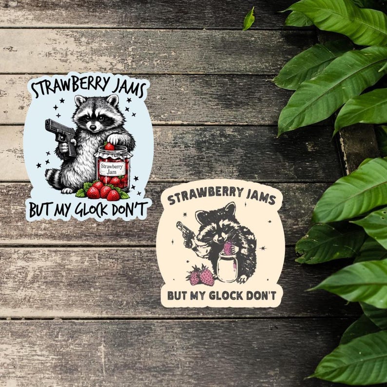 May include: Two stickers featuring a raccoon with a gun and a jar of strawberry jam. One sticker has a light blue background with the text "STRAWBERRY JAMS" and "BUT MY GLOCK DON'T". The other sticker has a tan background.