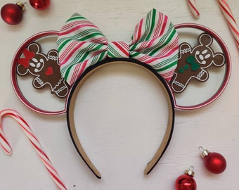 May include: Red and green striped bow headband with gingerbread man ornaments. The headband is on a white surface with red ornaments and candy canes.