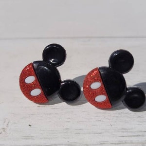 K&ouml;nnte beinhalten: Ein Paar Ohrringe in Form von Mickey Mouse. Jeder Ohrring hat einen schwarzen Kopf mit zwei kleinen schwarzen Ohren und einem roten, glitzernden Gesicht mit zwei wei&szlig;en Ovalen. Die Ohrringe sind vor einem wei&szlig;en Hintergrund platziert.