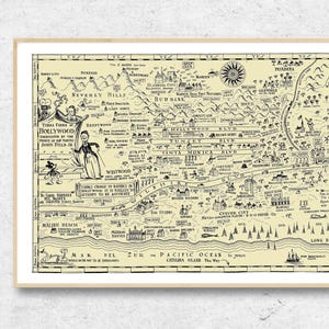 May include: A framed vintage map of Los Angeles, California, in a cream and black color scheme. The map features illustrations of landmarks and text including "Hollywood" and "Pacific Ocean". The map is displayed on a white wall.