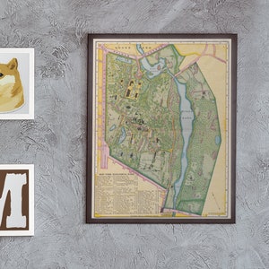 May include: A living room interior with a gray sofa, a pink throw blanket, a black shelf with books, a record player, and a mirror. There are three framed pictures on the wall: a map, a dog, and a letter M.
