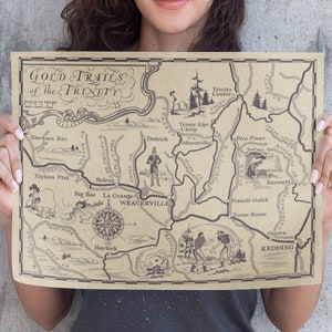 May include: A vintage-style map of the Gold Trails of the Trinity, California. The map is printed on brown paper and features hand-drawn illustrations of mountains, rivers, and towns. The map includes the names of locations such as Hawkins Bar, Taylors Flat, Dedrick, Trinity Centre, Trinity Alps Camp, Minersville, Five Pines, Kennett, French Gulch, Tower House, Shasta, Redding, La Grange, Weaverville, and Hayfork.