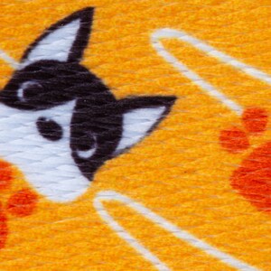 May include: A yellow fabric with a white and black dog face and orange paw prints. The fabric has a textured surface.
